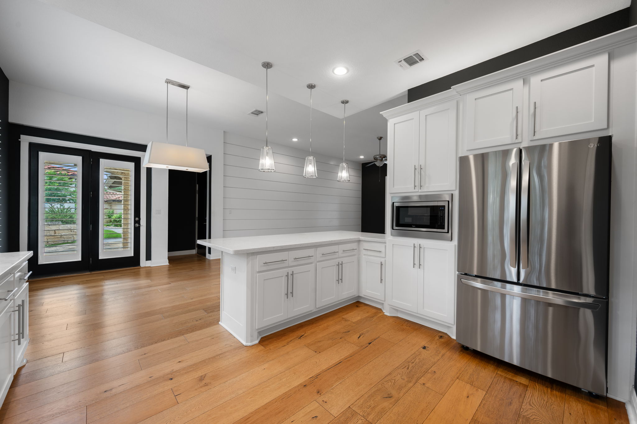 13708 Golden Wave Loop Austin, TX 78738 - Photo 10 of 34 Bright kitchen featuring hardwood floors, white cabinetry, a large kitchen island with pendant lighting, and stainless steel appliances including a refrigerator and built-in microwave