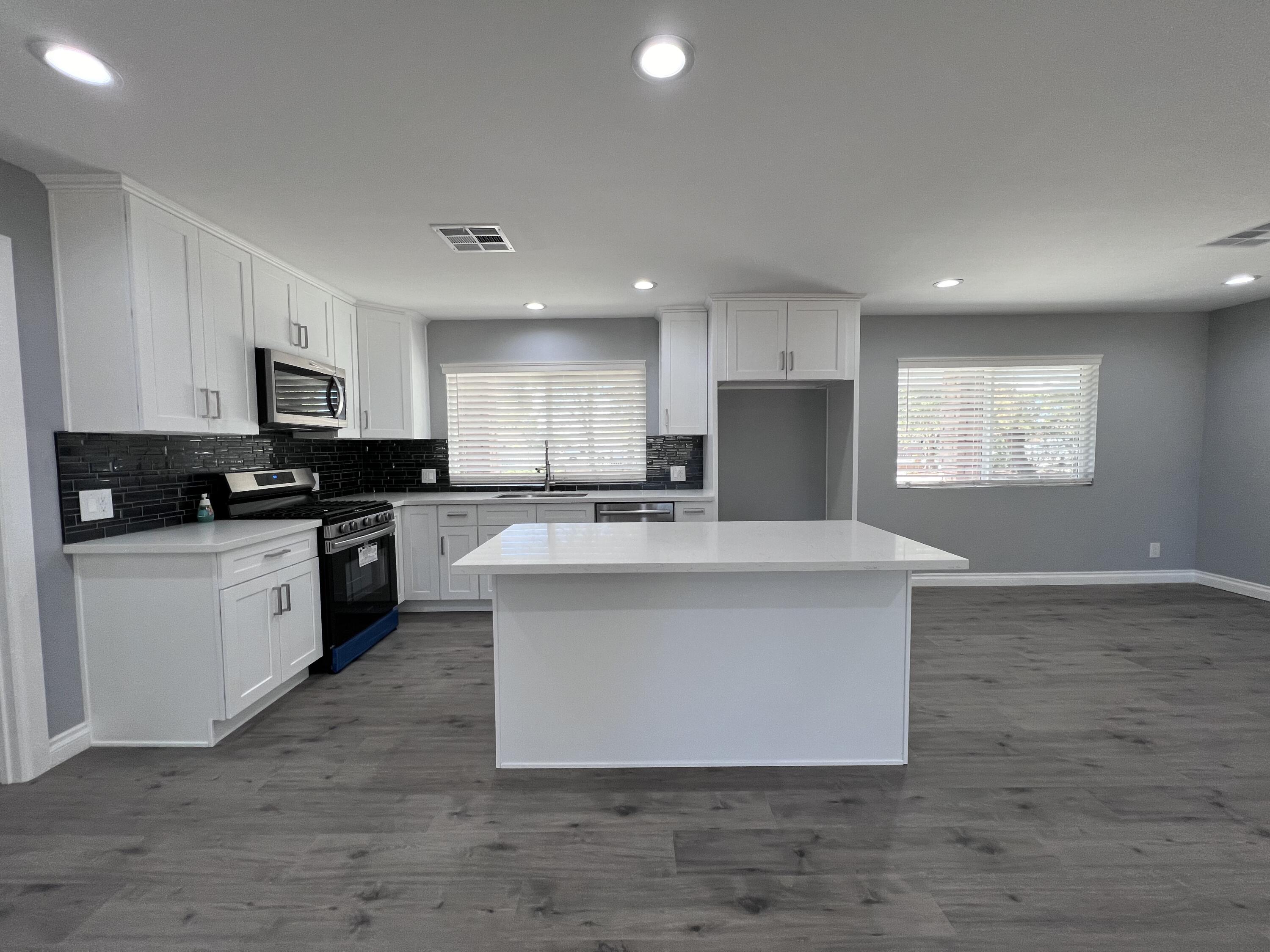 3255 East E Avenue Lancaster, CA 93535 - Photo 25 of 81 a large white kitchen with kitchen island granite countertop a stove top oven a sink dishwasher and a refrigerator with wooden floor