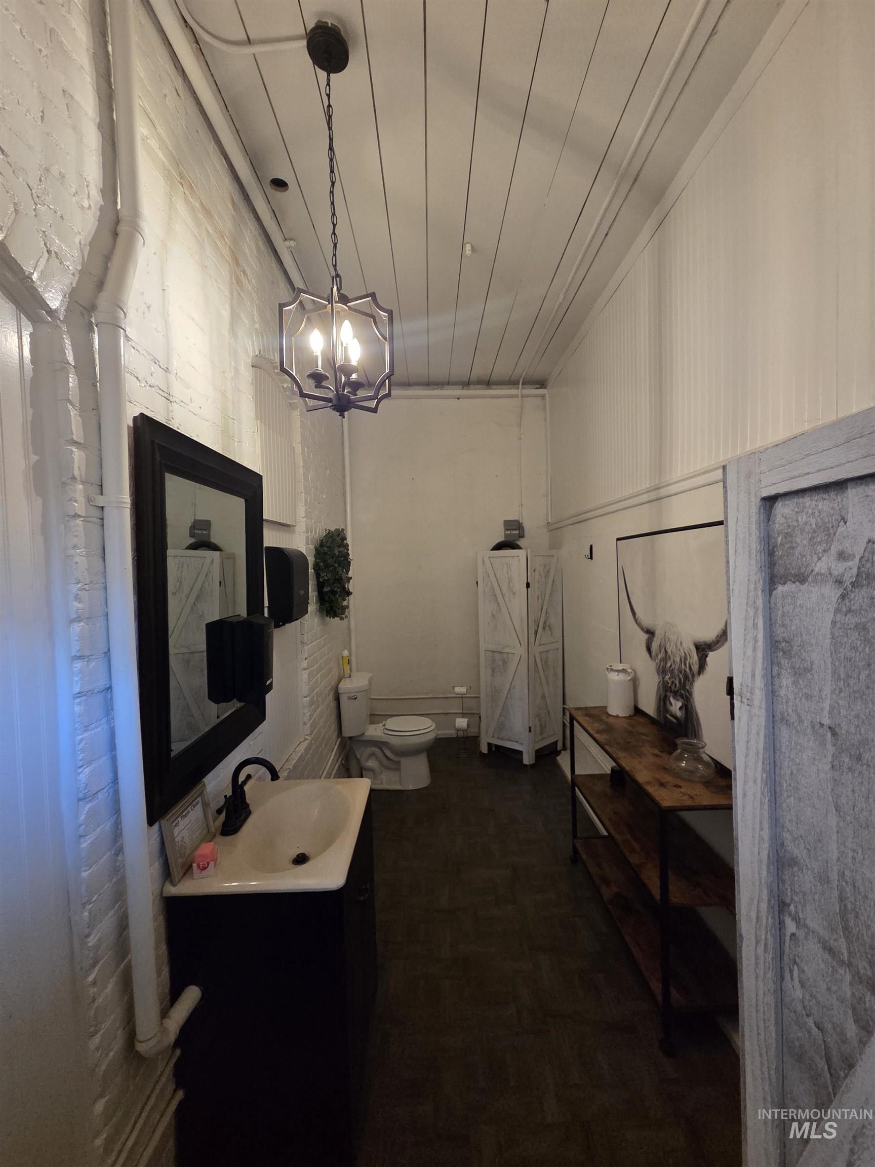 847 Main Street Pomeroy, WA 99347 - Photo 11 of 12 Modern washroom with a black vanity sink, wall-mounted mirror, dark wood-finish flooring, and a decorative ceiling light fixture