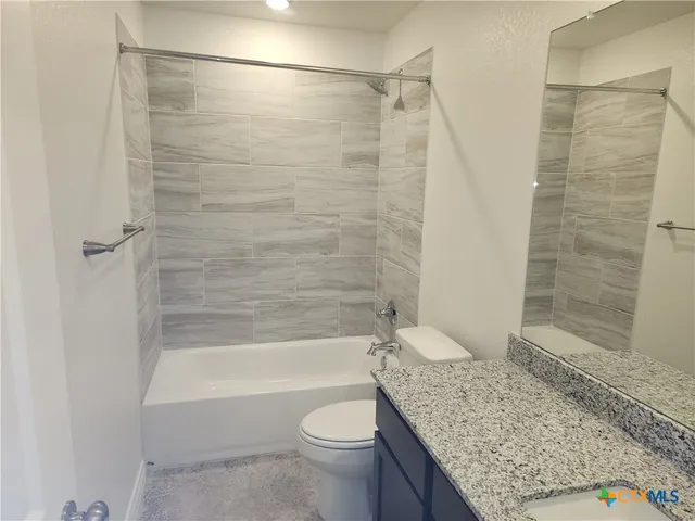 a bathroom with a granite countertop bathtub shower sink vanity and toilet