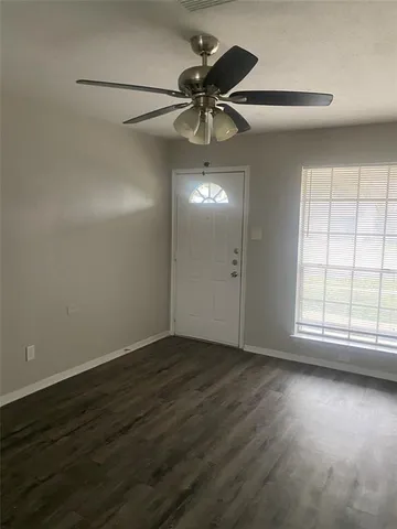 an empty room with wooden floor fan and windows