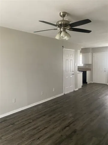 a view of an empty room with wooden floor and a ceiling fan
