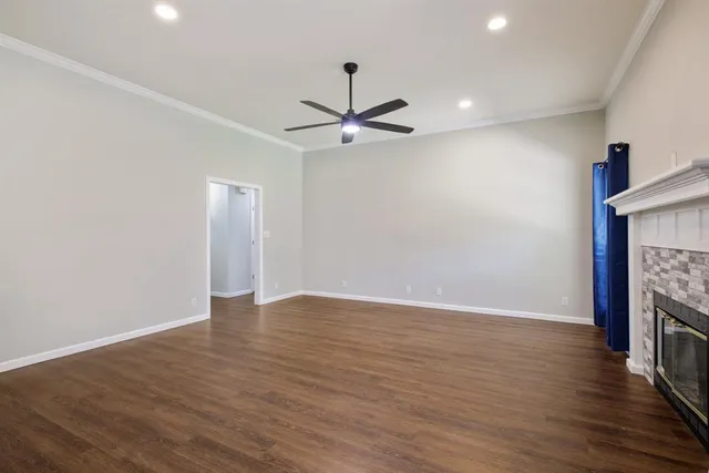 a view of an empty room with wooden floor a ceiling fan and a fireplace