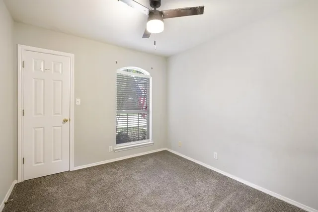 an empty room with chandelier fan and windows