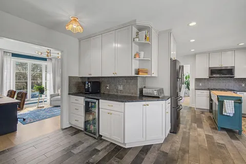 a large kitchen with stainless steel appliances granite countertop a stove a sink a refrigerator and white cabinets with wooden floor