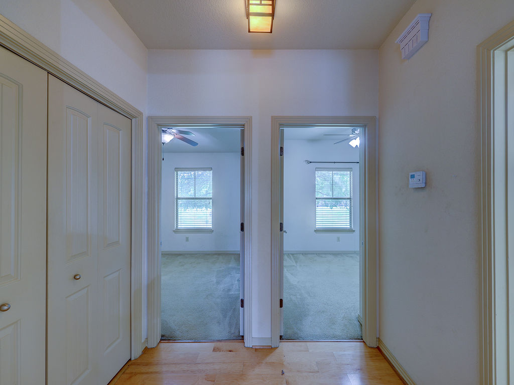 9707 Anderson Mill Road, Unit 22 Austin, TX 78750 - Photo 20 of 39 A well-lit hallway with natural hardwood flooring connects two carpeted bedrooms, each featuring a ceiling fan and window.