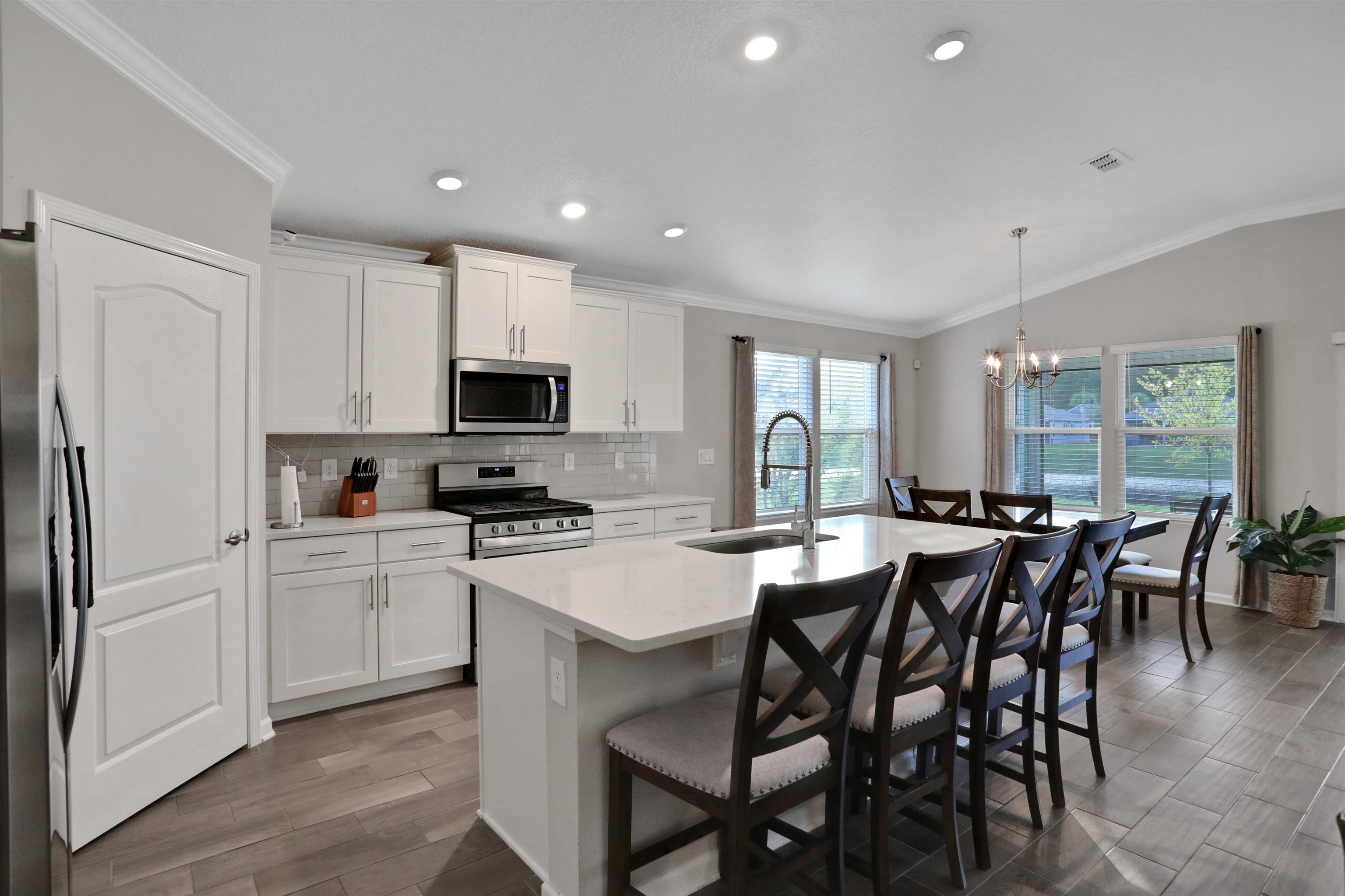 Undisclosed Address St. Augustine, FL 32095 - Photo 17 of 51 Kitchen featuring crown molding, decorative backsplash, a center island with sink, white cabinets, and a kitchen bar