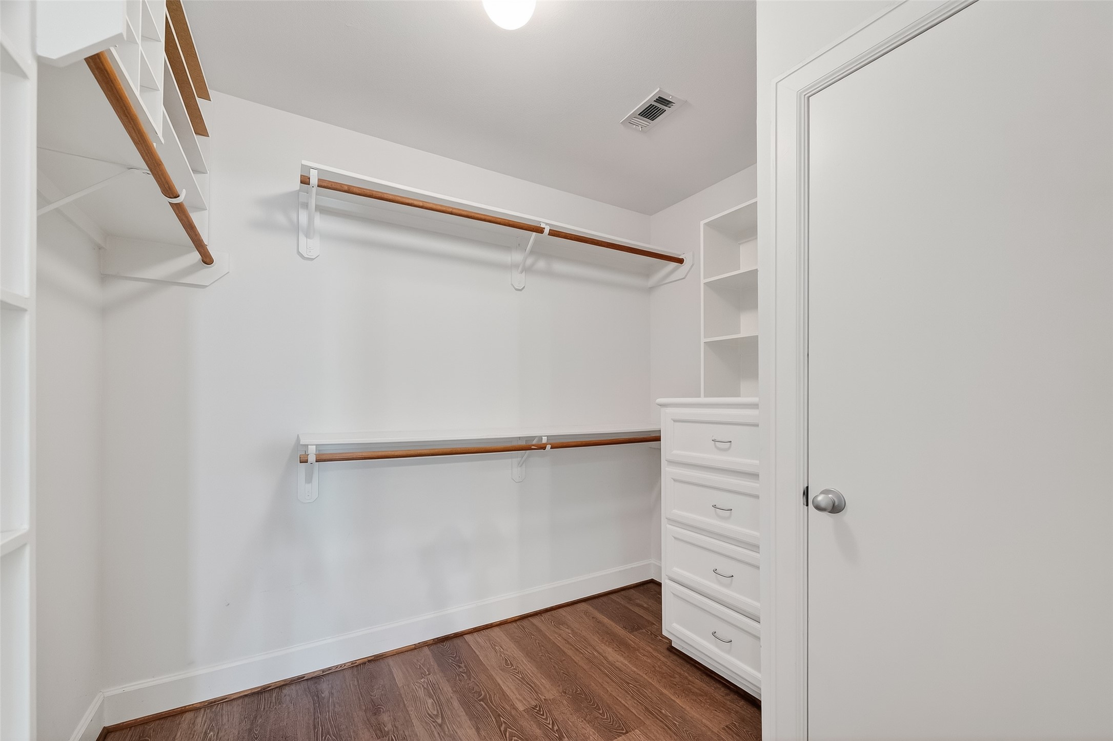 5951 S Loop East, Unit 47 Houston, TX 77033 - Photo 19 of 37 Primary bedroom has a spacious walk-in closet with wooden floors, ample hanging space, built-in shelves, and drawers. The bright lighting and white walls create an open, airy feel.
