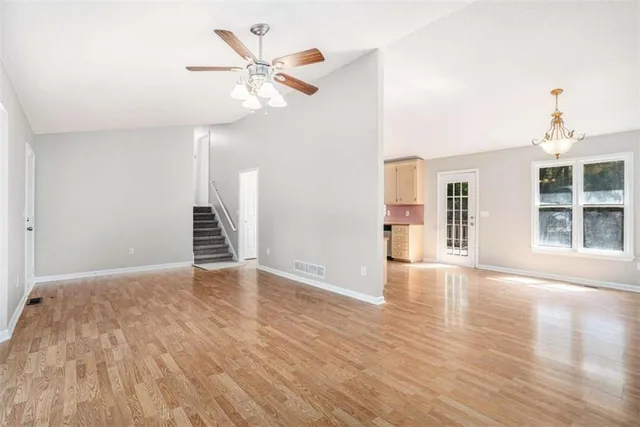 a view of an empty room with wooden floor and a ceiling fan