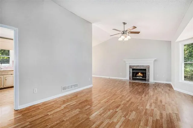 a view of a room with a fireplace a ceiling fan and wooden floor