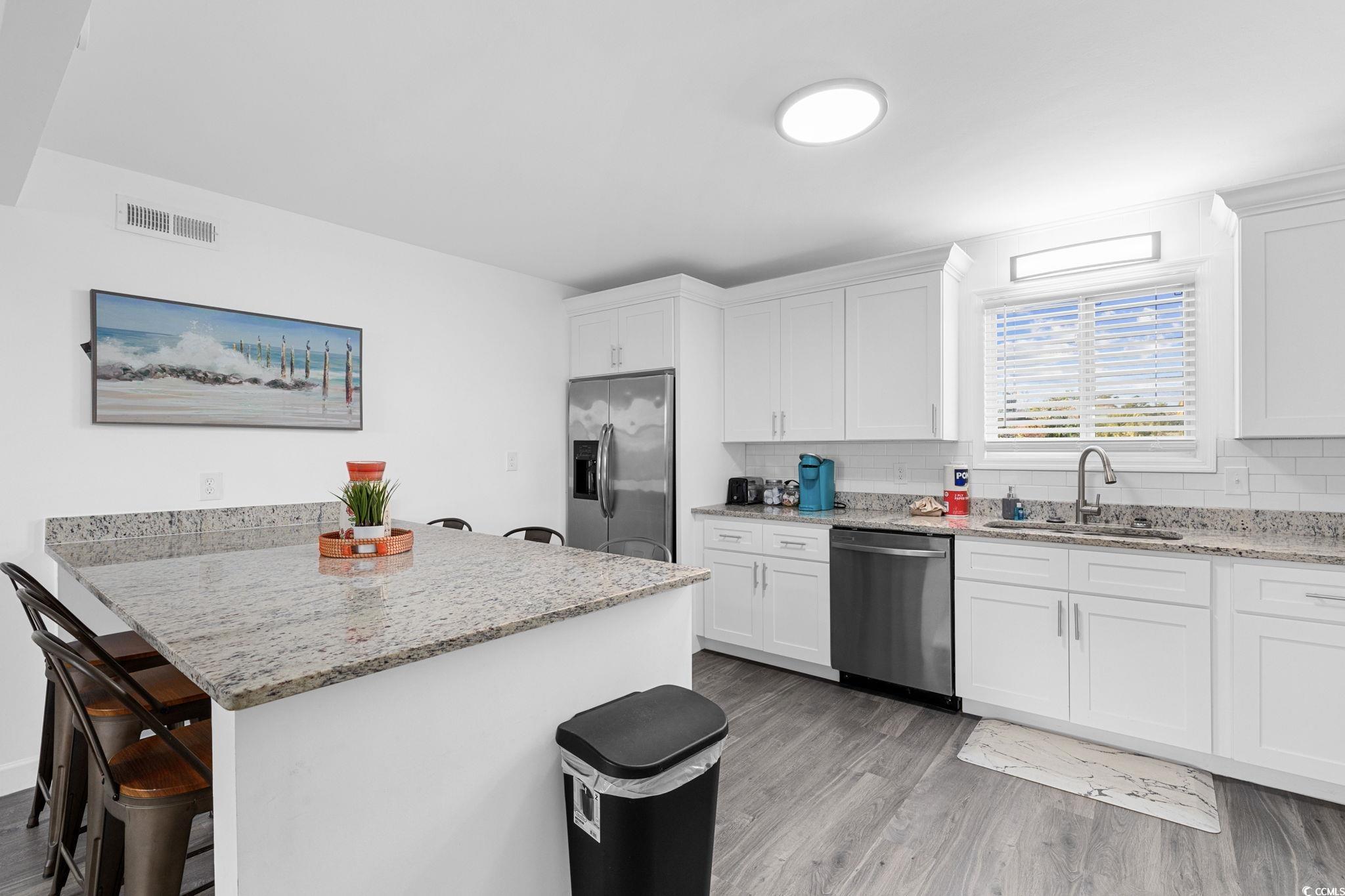 409 17th Avenue North, Unit 3 Myrtle Beach, SC 29577 - Photo 9 of 16 Kitchen with a kitchen breakfast bar, light stone counters, light wood-style floors, and appliances with stainless steel finishes