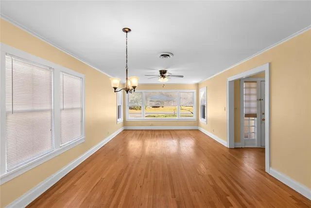 a view of an empty room with window wooden floor and a kitchen view