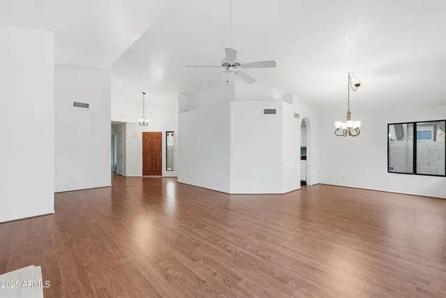 a view of an empty room with wooden floor and a ceiling fan