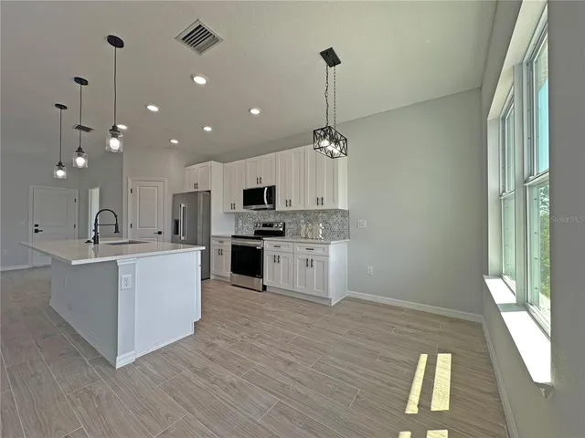 a large kitchen with white cabinets stainless steel appliances a sink and wooden floor