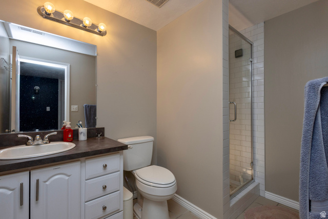 11751 Lake Run Road South Jordan, UT 84009 - Photo 31 of 38 Bathroom featuring a glass-enclosed shower with subway tile surround, a single vanity with an integrated sink, a dark countertop, white cabinetry with silver-tone hardware, and a wall-mounted light fixture