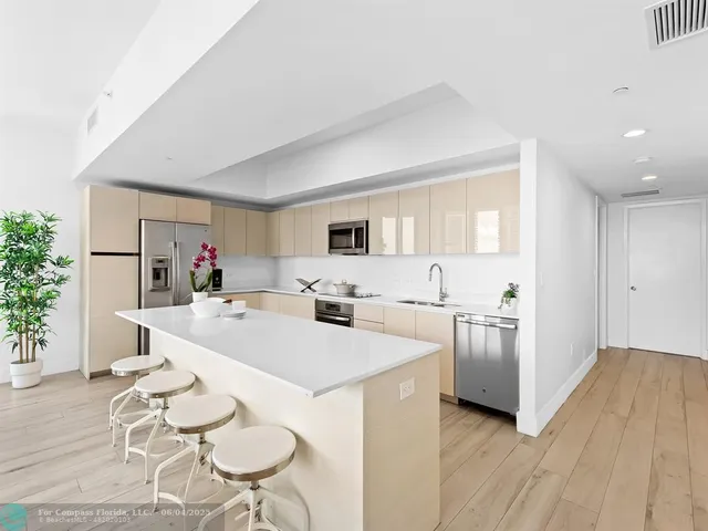 a large white kitchen with stainless steel appliances kitchen island granite countertop a table chairs and a refrigerator