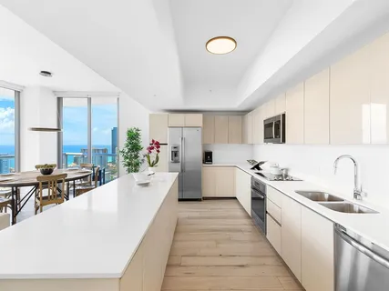 a large white open kitchen with stainless steel appliances kitchen island a large counter top a sink and cabinets