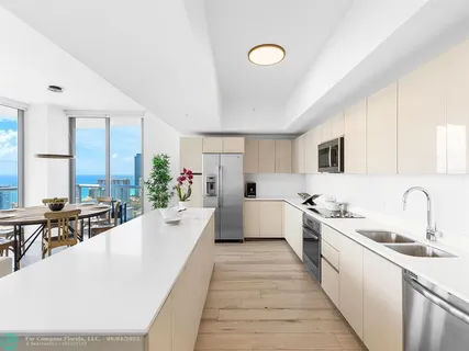 a large white open kitchen with stainless steel appliances kitchen island a stove a sink dishwasher and white cabinets with wooden floor