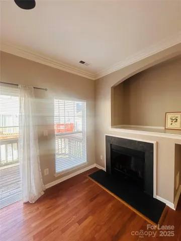 a view of an empty room with wooden floor fireplace and a window