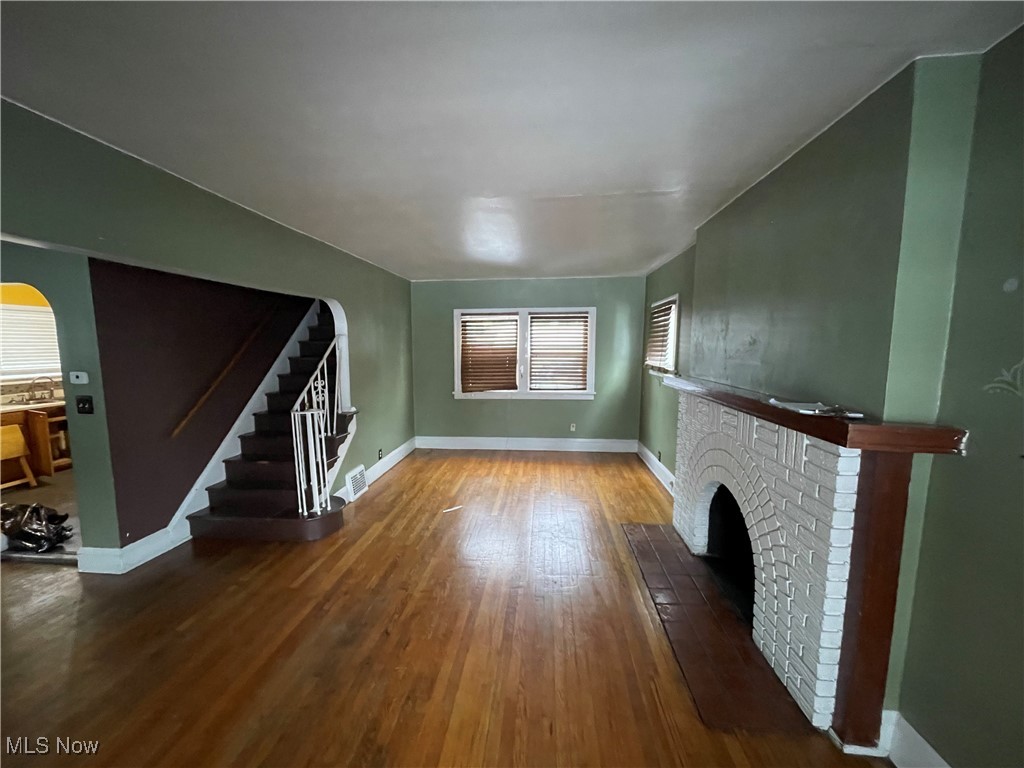 3544 Silsby Road Cleveland, OH 44118 - Photo 3 of 19 Unfurnished living room with arched walkways, a brick fireplace, dark wood-style flooring, stairs, and plenty of natural light