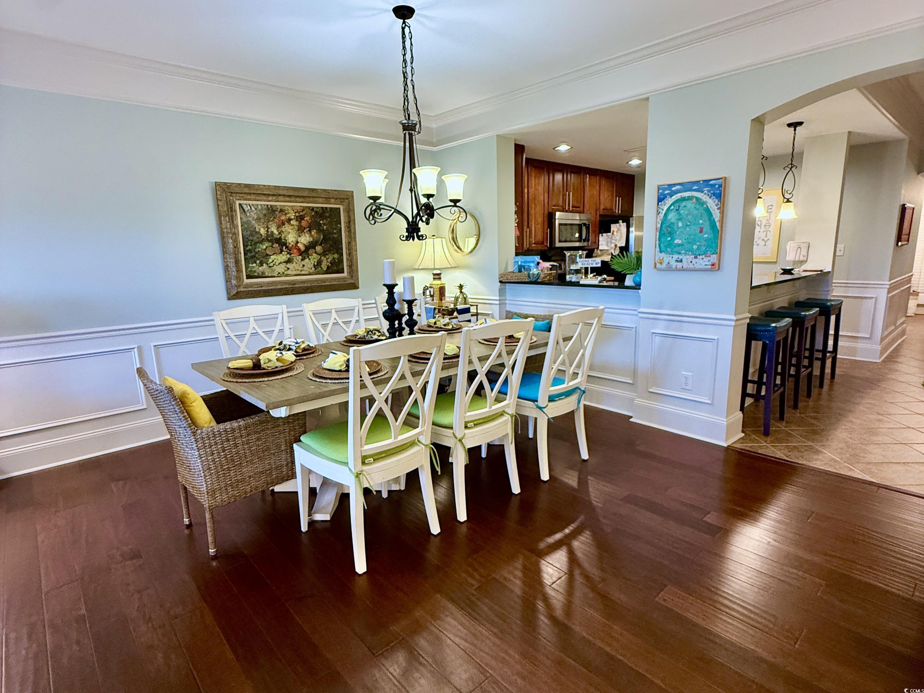 1330 Villa Marbella Court, Unit 303 Myrtle Beach, SC 29572 - Photo 6 of 40 Dining area with a decorative wall, arched walkways, a wainscoted wall, wood finished floors, and crown molding