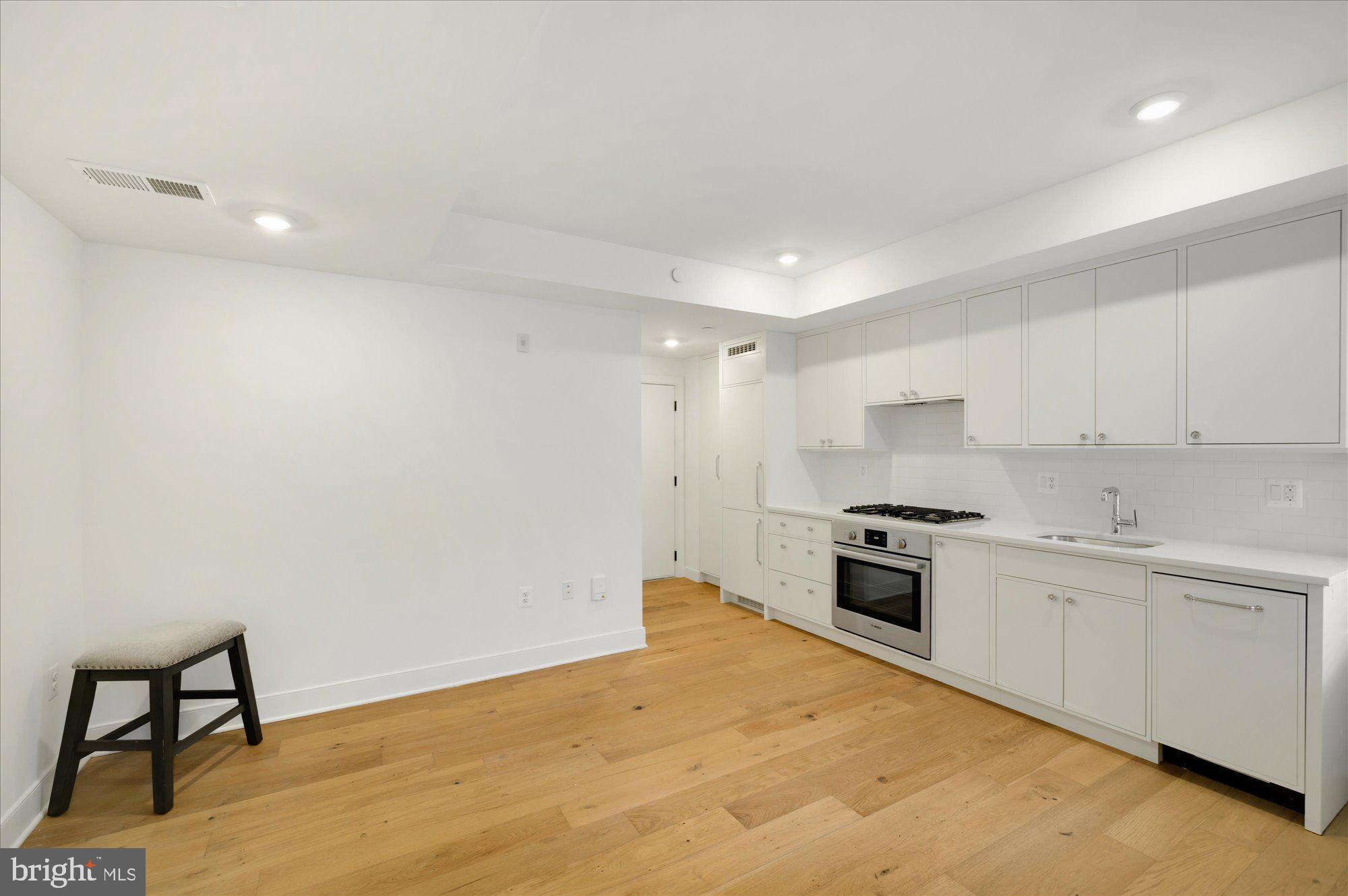 2869 28th Street Northwest, Unit 103 Washington, DC 20008 - Photo 13 of 19 a large kitchen with stainless steel appliances granite countertop a stove a sink a refrigerator and white cabinets with wooden floor