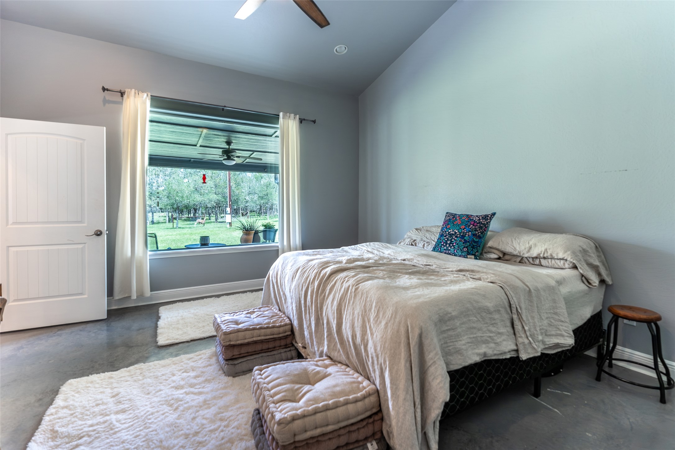 4082 Old Colony Line Road Lockhart, TX 78644 - Photo 6 of 40 A spacious bedroom with a panoramic window frames serene garden vistas, offering a peaceful retreat.