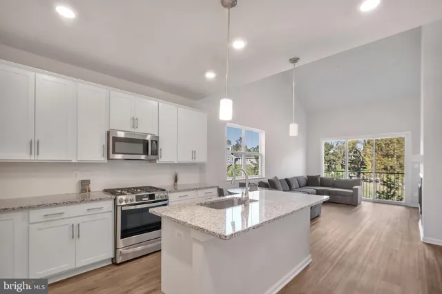 a kitchen with stainless steel appliances granite countertop a sink dishwasher stove and white cabinets with wooden floor