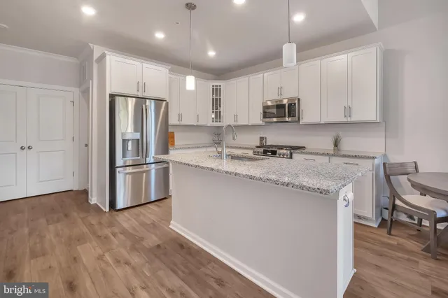 a kitchen with kitchen island granite countertop a refrigerator a stove a sink and white cabinets with wooden floor