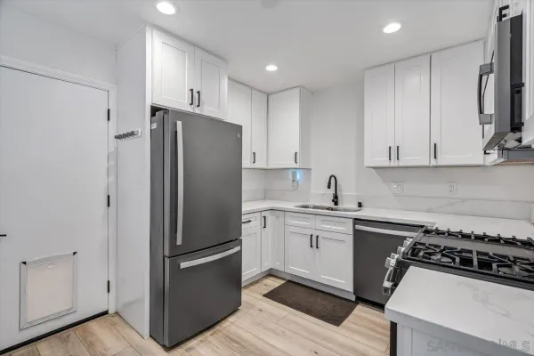 a kitchen with stainless steel appliances a refrigerator a sink and white cabinets