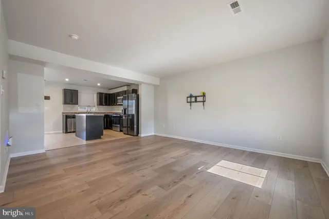 a view of empty room with wooden floor and kitchen
