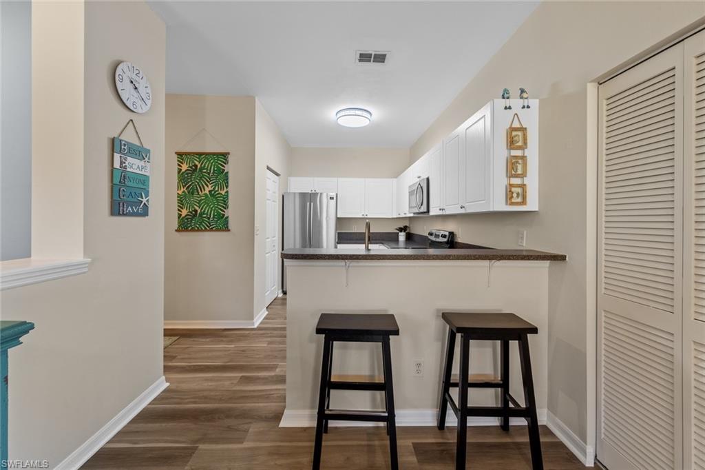 4306 Bellasol Circle, Unit 3422 Fort Myers, FL 33916 - Photo 12 of 41 Kitchen with dark countertops, white cabinets, dark wood-style floors, a peninsula, and a breakfast bar area