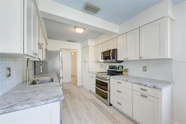 a kitchen with granite countertop a sink stainless steel appliances and white cabinets