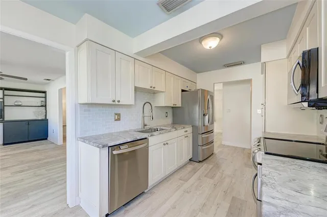 a kitchen with stainless steel appliances granite countertop a stove top oven a refrigerator and white cabinets with wooden floor