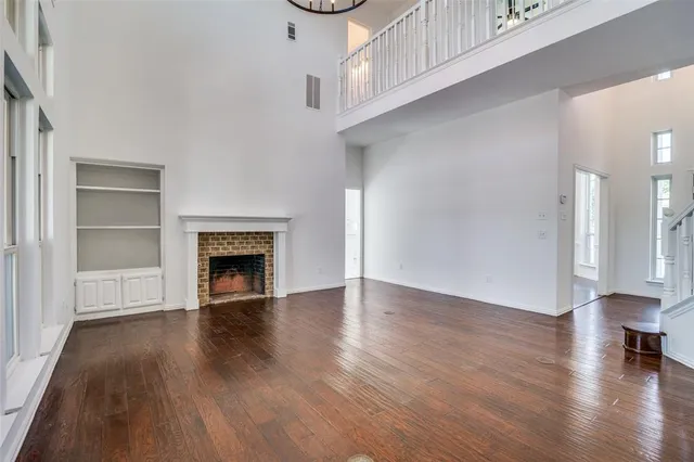 a view of an empty room with wooden floor fireplace and a window