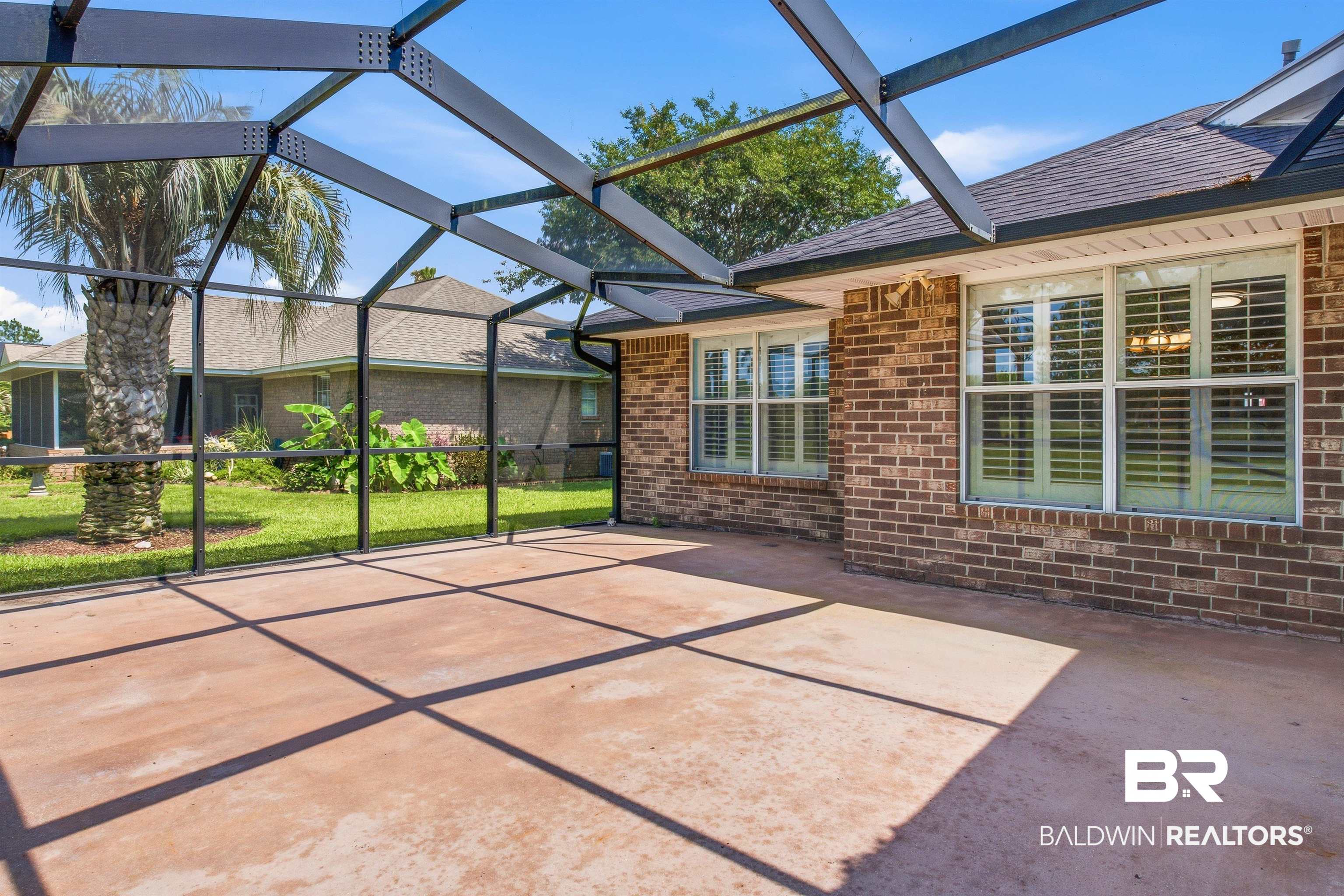 22685 County Road 12 Foley, AL 36535 - Photo 16 of 89 Screened patio with a concrete floor, brick exterior, multiple windows with interior blinds, and a surrounding lawn with a mature palm tree