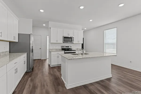 a kitchen with stainless steel appliances a stove top oven a sink a refrigerator white cabinets and wooden floor