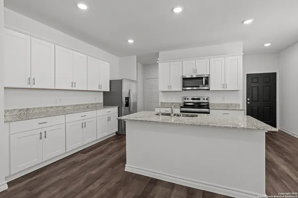 a kitchen with granite countertop a refrigerator stove a sink and white cabinets