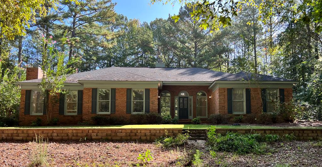 a view of a brick house with a yard plants and large trees