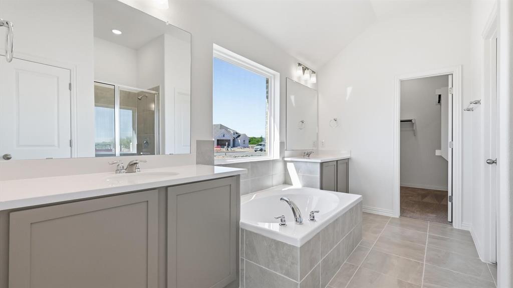 2529 Rivers W Road Anna, TX 75409 - Photo 30 of 40 Spacious bathroom featuring a built-in soaking tub with tiled surround, dual vanities with integrated sinks, and ample natural light from a large window