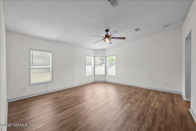 a view of empty room with wooden floor and fan