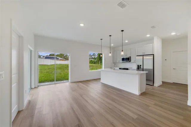a view of an empty room with kitchen and a window