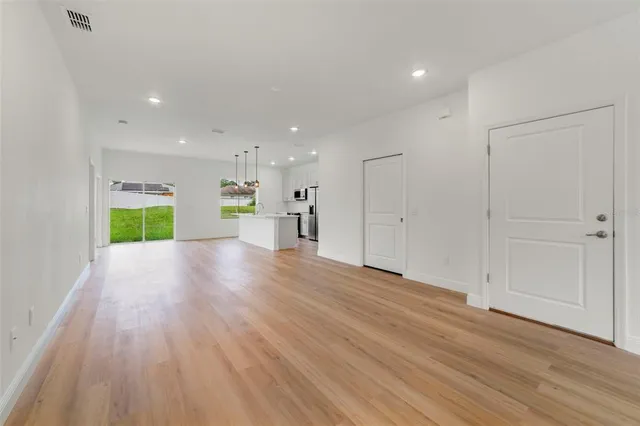 a view of an empty room with wooden floor kitchen view and a window