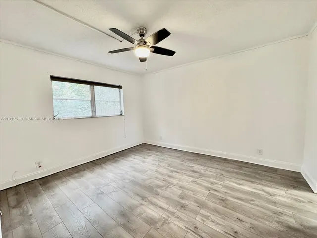 an empty room with wooden floor fan and windows
