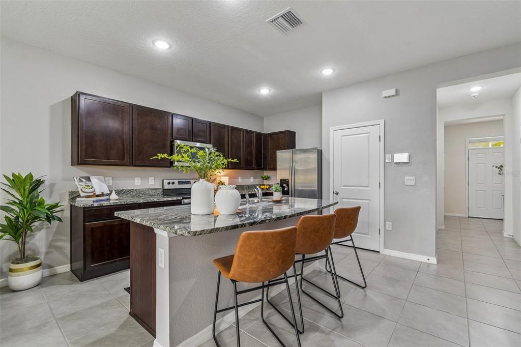 33083 Frosted Clover Way Wesley Chapel, FL 33545 - Photo 3 of 70 a kitchen with stainless steel appliances kitchen island granite countertop a sink a stove a refrigerator cabinets and chairs