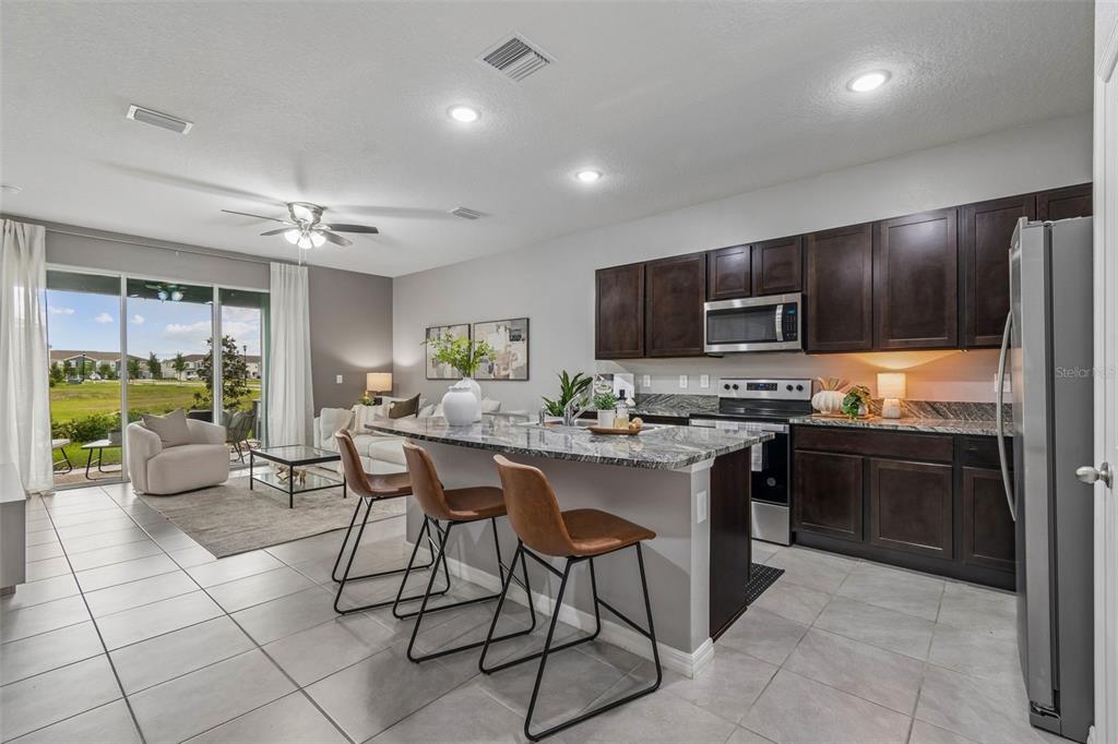 33083 Frosted Clover Way Wesley Chapel, FL 33545 - Photo 5 of 70 a kitchen with stainless steel appliances granite countertop a stove top oven a sink dishwasher a dining table and chairs with wooden floor