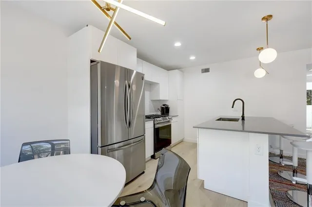 a kitchen with stainless steel appliances granite countertop a refrigerator a sink dishwasher a stove with white cabinets and wooden floor