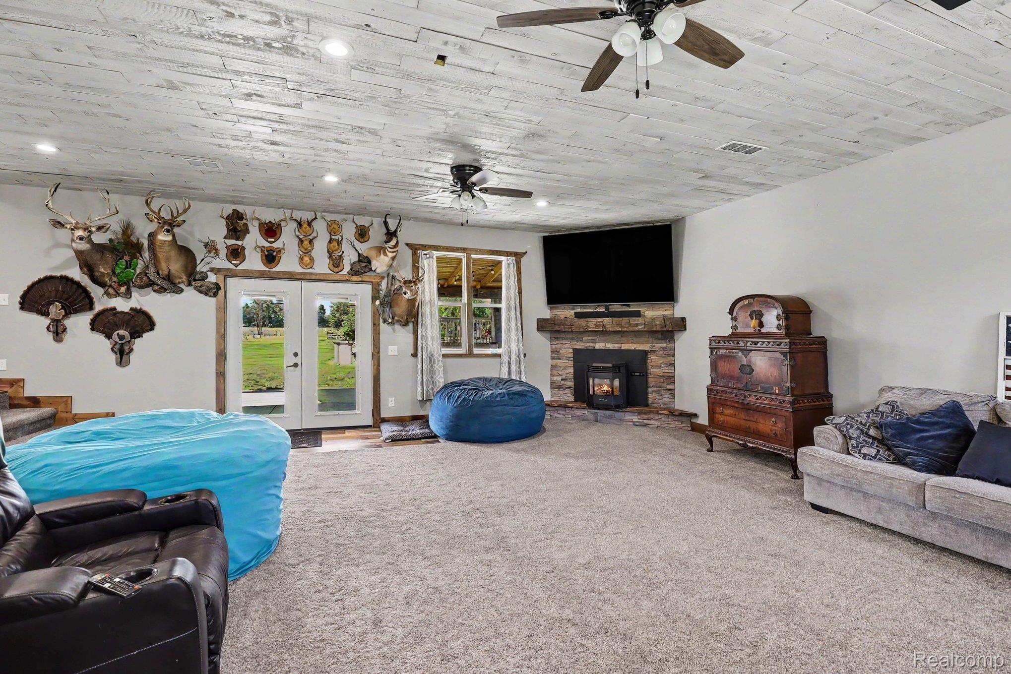 2150 East Snover Road Mayville, MI 48744 - Photo 9 of 48 Spacious living area featuring a stone-clad fireplace with hearth, wood-finish plank ceiling, recessed lighting, and dual ceiling fans