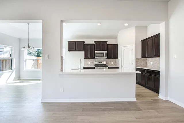 a open kitchen with stainless steel appliances kitchen island granite countertop a refrigerator stove top oven and sink with wooden floor