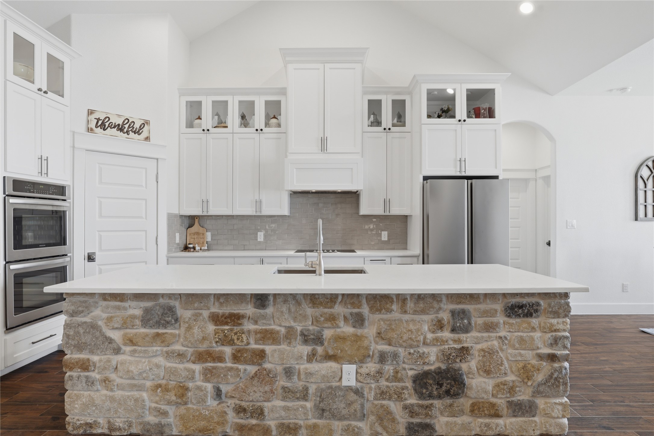 133 Greg Lane Jarrell, TX 76537 - Photo 9 of 24 Kitchen featuring a stone-clad island with a light-toned countertop, white cabinetry with glass accents, stainless steel appliances, and a vaulted ceiling